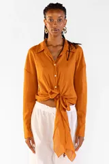 Camisa de algodón color tostado, de manga larga, con cuello camisero, botones frontales y detalle de lazo ajustable en la cintura.