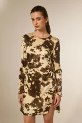 Vestido corto de manga larga con cuello redondo, confeccionado en tela satinada con estampado animal print tipo vaca. Presenta un diseño al cuerpo con pinzas y una abertura lateral en la falda.