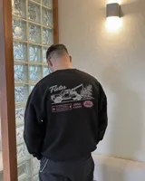 Buzo negro de cuello redondo y manga larga, de corte regular fit. En la espalda presenta un estampado gráfico en color blanco y rosa con la leyenda "Fletes" y el dibujo de una grúa transportando una planta.