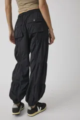 Pantalón jogger negro de inspiración utility, confeccionado en tejido liviano de poliamida. Cuenta con cintura elástica ajustable con cordón, bolsillos cargo con broches metálicos, diseño con paneles fruncidos y puños elastizados.