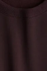 Buzo de tejido liso color borgoña oscuro, con cuello redondo, hombros caídos y puños y bajo acanalados.