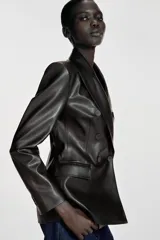 Blazer de corte cruzado confeccionado en material efecto piel, con cuello de solapa, manga larga con hombreras y cierre frontal con botones. Presenta bolsillos delanteros con solapa.