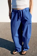 Pantalón cargo de tiro medio con corte oversize, bolsillos laterales con solapa en las piernas y bolsillos de plastrón en el delantero. Cuenta con trabillas, lazadas ajustables en la cintura y cierre frontal con cremallera y botón.