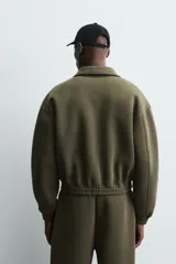 Cazadora de corte boxy fit confeccionada en tejido técnico compacto de algodón con elasticidad. Presenta cuello solapa, cierre frontal con cremallera, bolsillos de vivo en la cadera y acabados elásticos en puños y bajo.