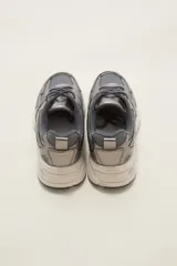 Zapatilla deportiva de estilo urbano en color blanco con detalles metalizados plateados y acentos en negro. Presenta una combinación de malla transpirable y paneles sintéticos, con suela robusta y cordones al tono.