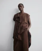 Vestido marrón de lino con escote en pico, manga sisa caída, volante con acabado desflecado en el delantero y cinturón. 