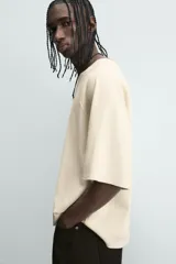 Camiseta de hombre, corte relaxed fit, color beige claro con textura. Presenta cuello redondo amplio y manga corta. Estampado frontal en negro con texto que incluye "Los Angeles".