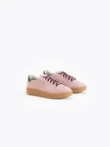 Zapatilla de cuero descarne color rosa, con suela de caucho color caramelo. Presenta cordones oscuros con un aplique de cristal decorativo y detalle de cuero liso en el talón.