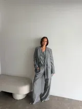 Conjunto sastrero de lino gris con rayas diplomáticas blancas, compuesto por un blazer oversize de botonadura simple, un chaleco entallado con botones y un pantalón sastrero de corte recto y holgado.