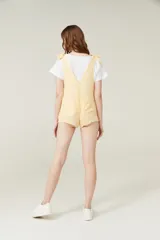 Mono corto color amarillo pastel, con breteles finos que se atan en los hombros, escote recto y dos bolsillos delanteros.