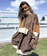 Buzo de estilo canguro con diseño de bloques de color y estampado animal print. Presenta una combinación de texturas en tonos marrón, chocolate y beige, con cuello alto, cierre frontal parcial con botones a presión y un bolsillo frontal grande con solapa.