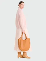 Bolso tipo tote de gran tamaño, confeccionado en cuero granulado color tostado. Presenta una silueta redondeada, asas superiores integradas con detalle de hebilla metálica dorada y un diseño minimalista y estructurado.