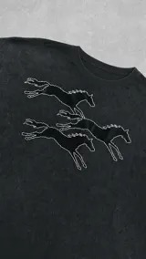 Remera de corte oversize color gris con efecto stone wash, manga corta y cuello redondo. Presenta una estampa frontal en serigrafía con el contorno de tres caballos en movimiento.