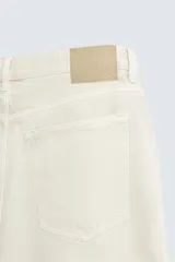 Bermuda de denim de algodón color beige claro, de corte regular fit y largo hasta la rodilla. Presenta cinco bolsillos y cierre frontal con cremallera y botón.