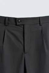 Pantalón de traje regular fit confeccionado en popelín de algodón. Presenta cintura con pliegues frontales, bolsillos laterales y bolsillos traseros de vivo con botón. El bajo tiene acabado con vuelta y el cierre es frontal con cremallera y botón.