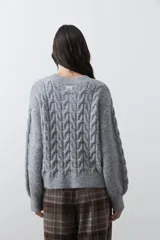 Cardigan de tejido de punto color marrón chocolate, con diseño de trenzas en el frente y mangas. Presenta cuello redondo, cierre frontal con botones al tono y puños acanalados.