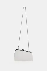 Bolso tipo clutch rígido de formato asimétrico con acabado metálico plateado. Incluye una cadena metálica fina extraíble para usar como bandolera y cierre mediante doble clip.