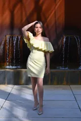 Vestido corto color amarillo manteca, con escote off-shoulder con volados y falda ajustada.