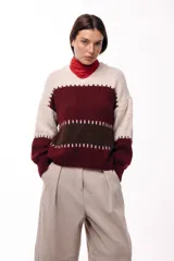 Sweater de tejido de punto grueso con diseño de bloques de color en tonos beige, marrón y bordó. Presenta un corte relajado, mangas amplias y detalles de costuras visibles en contraste que separan las franjas de color.
