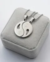 Dije de acero inoxidable con diseño de Yin-Yang, compuesto por dos piezas complementarias que forman un círculo completo, cada una con un símbolo de Yin-Yang grabado.