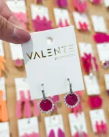 Aros colgantes con argolla de acero plateado y dije circular fucsia con borde de strass.