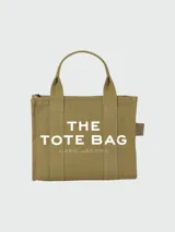 Bolso tipo tote de Marc Jacobs, confeccionado en lona resistente color beige. Presenta el logo estampado en contraste en el frente, doble asa superior y cierre superior con cremallera.