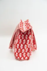 Bolso tipo tote acolchado con estampado floral en tonos rojizos, rosados y verdes. Presenta asas de mano con diseño de rayas verticales en color rojo y blanco, y ribetes a juego en los bordes.