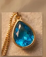 Collar de bronce con cadena fina eslabonada y dije en forma de gota con piedra color azul zafiro.