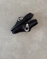 Suecos negros de cuero con hebilla plateada decorativa.