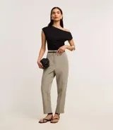 Pantalón de sastrería corte carrot, color beige, con cintura alta, pinzas frontales y cinturón fino incorporado con hebilla metálica.