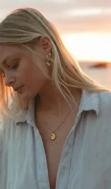 Collar de acero dorado con cadena fina eslabonada con pequeñas cuentas esféricas y un dije colgante en forma de caracol marino.