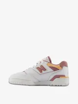 Championes urbanos New Balance modelo 550, color blanco con detalles en rosa y amarillo, confeccionados en cuero sintético, con logo "N" característico en los laterales.