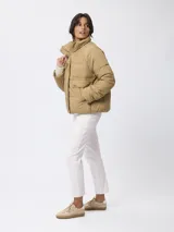 Campera puffer color beige con cuello alto, cierre frontal con cremallera y botones a presión, bolsillos frontales con solapa y diseño acolchado.