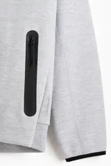 Campera bomber deportiva gris melange, de corte estándar, con cuello elevado corto, cierre bidireccional y mangas raglán. Posee bolsillos delanteros con cierre y costuras selladas, además de elástico fino en puños y bajo.