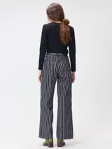 Pantalón de tiro medio y pierna ancha confeccionado en denim de algodón grueso. Presenta un diseño a rayas verticales en tonos azul y celeste, con costuras en contraste color rojo, bolsillos laterales tipo cargo y remaches metálicos.