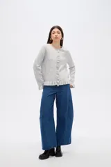Saco de punto color gris, con cuello redondo, cierre frontal con botones y detalle de volados en la tapeta y el ruedo. Presenta mangas largas con puños acampanados.