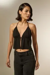 Top negro con escote en V profundo y diseño halter, confeccionado en tejido con sutiles detalles de strass. Presenta un corte holgado con una abertura central y frunces bajo el busto.