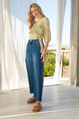 Blusa cruzada con estampado floral en tonos de lila, amarillo y verde. El cruce se ajusta a la cintura con un lazo. Tiene mangas 3/4 con puños elásticos y escote en V.