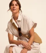 Vestido midi camisero de tricolina con estampado de rayas verticales finas en tonos beige y blanco. Tiene cuello solapa, mangas cortas con puños, abotonadura frontal y corte a la cintura.