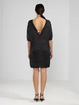Vestido corto de punto con hilos metálicos que aportan un brillo sutil. Presenta un calce relajado, cuello redondo, mangas cortas y espalda en V pronunciada con detalle de dije metálico.