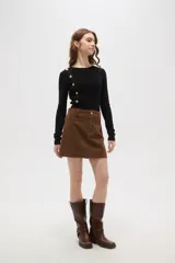 Falda mini de corte recto confeccionada en pana de algodón color verde oliva, con cierre frontal de botón metálico y pasacintos.