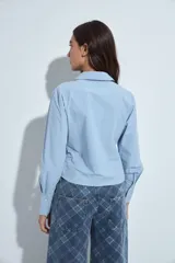 Camisa blanca de manga larga con cuello clásico y cierre frontal de botones. Presenta un diseño entallado con frunces decorativos en la parte central delantera.