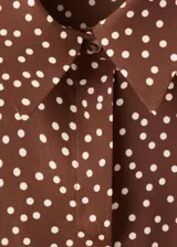 Camisa de poliéster color marrón con estampado de lunares blancos, cuello camisero, manga larga y cierre frontal de botones ocultos.