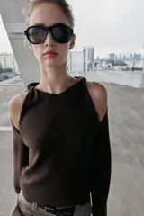 Jersey de punto color marrón oscuro, con cuello redondo y manga larga. Presenta un diseño con aberturas y nudos decorativos en los hombros.