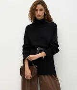 Suéter de punto color negro, con diseño oversize y largo alargado. Presenta cuello alto, mangas largas con puños acanalados y acabado acanalado en el ruedo.