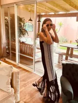 Vestido largo tejido en lurex color beige con diseño vertical y terminación en flecos negros. Breteles finos de cuero intervenido a mano con tientos de cuero plateado.