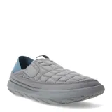 Championes tipo mocasín slip-on Merrell Hut Moc 2, color gris con diseño acolchado tipo matelassé. Presenta talón colapsable, suela de EVA ligera y detalles en azul en la parte posterior.