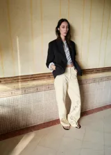 Jeans de tiro alto color beige con diseño recto, cinco bolsillos y detalles bordados calados en la parte inferior de las piernas.