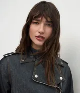 Campera estilo biker confeccionada en denim oscuro, con diseño estructurado, cuello con solapas, cierre frontal asimétrico y botones a presión metálicos.