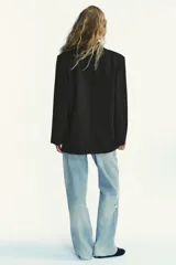 Blazer negro de corte oversize, con cuello solapa, escote pico, manga larga con hombreras y forro interior. Presenta bolsillos con solapa delanteros y bolsillo de vivo en el pecho.